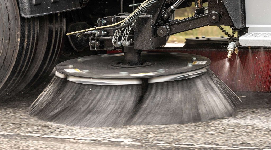 A brush on a sweeping truck cleaning a street